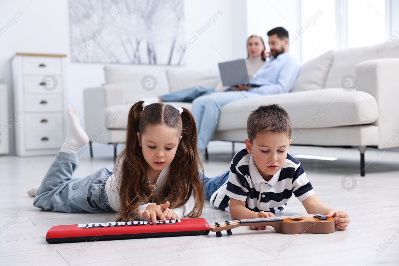 Kids playing with toys near their parents on warm floor at home, selective focus. Heating system Photo of Kids playing with toys near their parents on warm floor at home, selective focus. Heating system