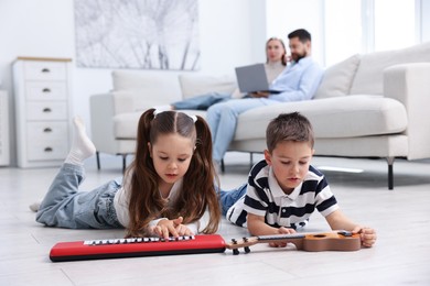 Photo of Kids playing with toys near their parents on warm floor at home, selective focus. Heating system