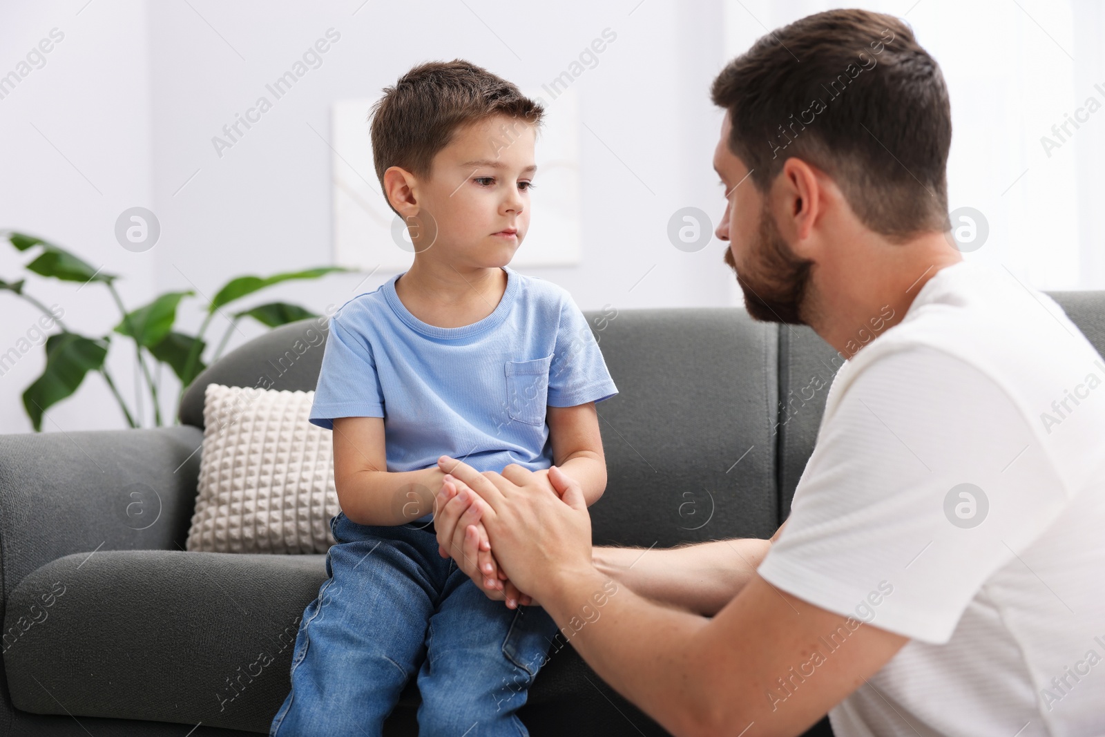 Father supporting his sad son on sofa at home Photo of Father supporting his sad son on sofa at home