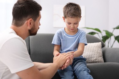 Photo of Father supporting his sad son on sofa at home