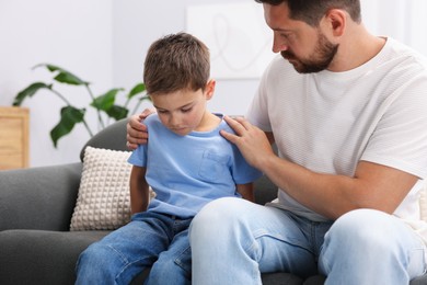 Photo of Father supporting his sad son on sofa at home