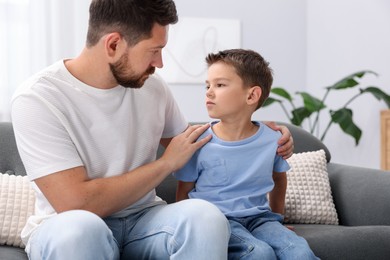 Photo of Father supporting his sad son on sofa at home