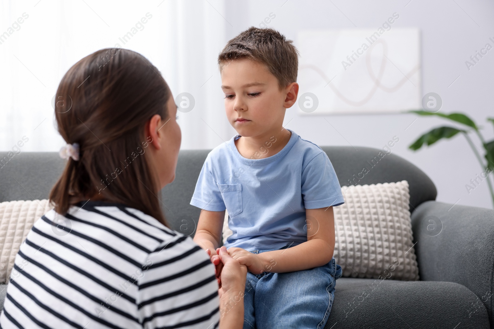 Mother supporting her sad son on sofa at home, space for text Photo of Mother supporting her sad son on sofa at home, space for text