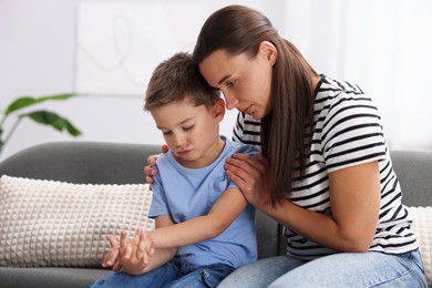 Photo of Mother supporting and hugging her sad son on sofa at home