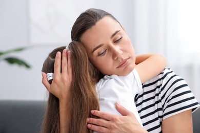 Photo of Mother supporting and hugging her sad daughter on sofa at home