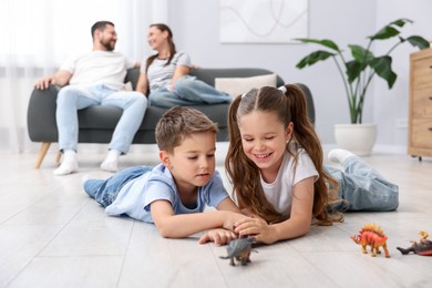 Photo of Kids playing with toys near their parents on warm floor at home, selective focus. Heating system