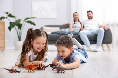 Photo of Kids playing with toys near their parents on warm floor at home, selective focus. Heating system