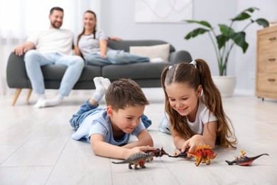 Photo of Kids playing with toys near their parents on warm floor at home, selective focus. Heating system