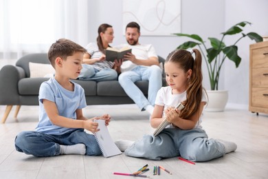 Photo of Kids drawing near their parents on warm floor at home, selective focus. Heating system