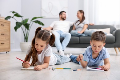 Photo of Kids drawing near their parents on warm floor at home, selective focus. Heating system