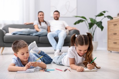 Photo of Kids drawing near their parents on warm floor at home, selective focus. Heating system