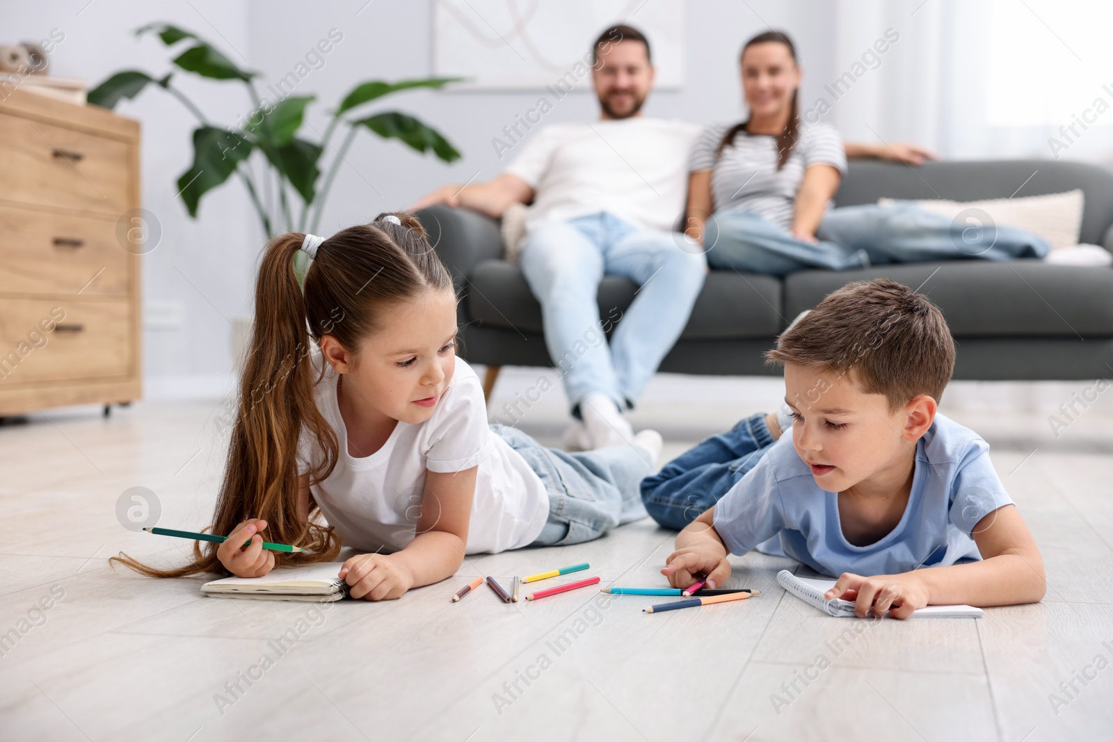 Photo of Kids drawing near their parents on warm floor at home, selective focus. Heating system