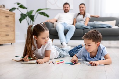Photo of Kids drawing near their parents on warm floor at home, selective focus. Heating system