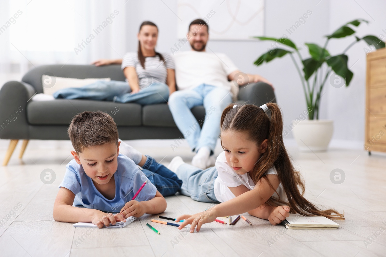 Photo of Kids drawing near their parents on warm floor at home, selective focus. Heating system