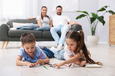 Photo of Kids drawing near their parents on warm floor at home, selective focus. Heating system