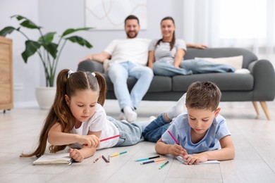 Photo of Kids drawing near their parents on warm floor at home, selective focus. Heating system