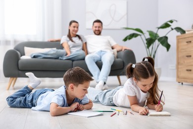 Photo of Kids drawing near their parents on warm floor at home, selective focus. Heating system