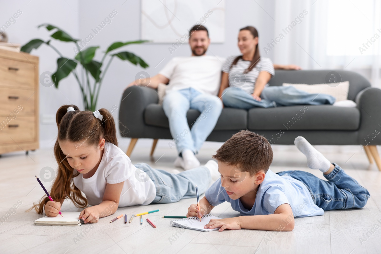Photo of Kids drawing near their parents on warm floor at home, selective focus. Heating system