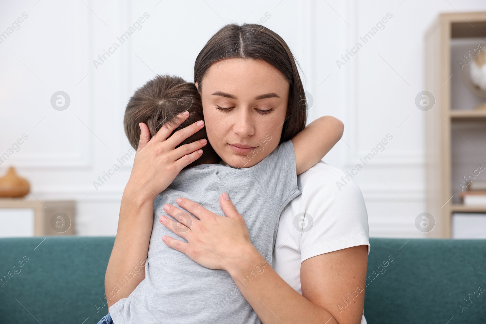 Photo of Mother supporting and hugging her sad son on sofa at home
