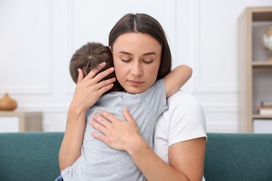 Photo of Mother supporting and hugging her sad son on sofa at home
