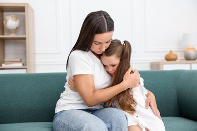 Photo of Mother supporting and hugging her sad daughter on sofa at home