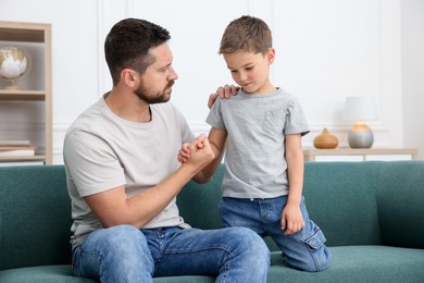 Photo of Father supporting his sad son on sofa at home