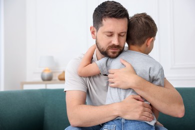 Photo of Father supporting his sad son on sofa at home