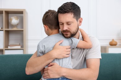 Photo of Father supporting his sad son on sofa at home