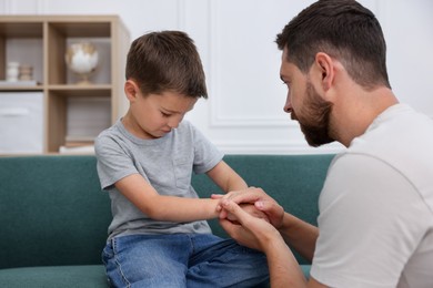 Photo of Father supporting his sad son on sofa at home