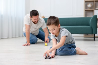 Photo of Father and his son playing with toys on warm floor at home, selective focus. Heating system
