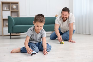 Photo of Father and his son playing with toys on warm floor at home, selective focus. Heating system