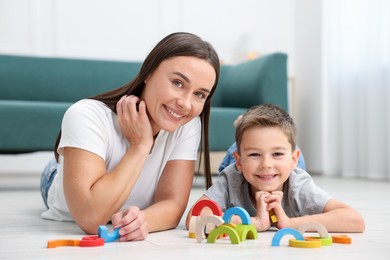 Photo of Mother and her son playing with toys on warm floor at home. Heating system