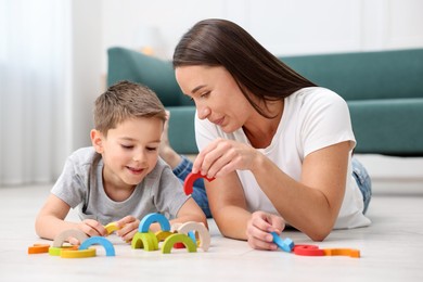Photo of Mother and her son playing with toys on warm floor at home. Heating system