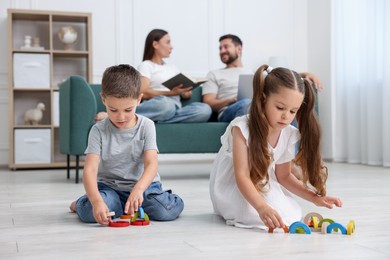 Photo of Kids playing with toys near their parents on warm floor at home, selective focus. Heating system