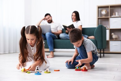 Photo of Kids playing with toys near their parents on warm floor at home, selective focus. Heating system