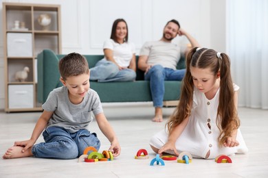 Photo of Kids playing with toys near their parents on warm floor at home, selective focus. Heating system