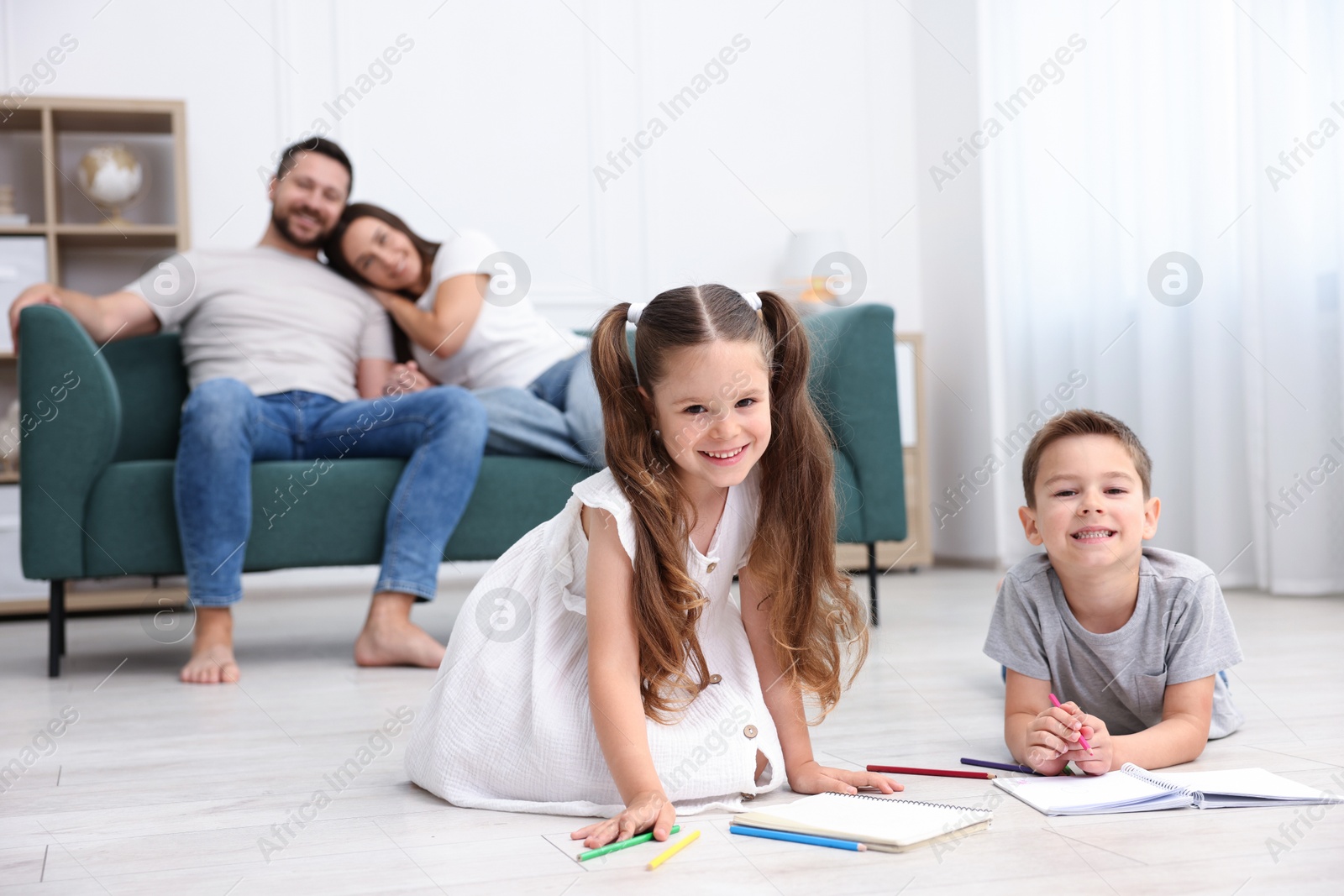 Photo of Kids drawing near their parents on warm floor at home, selective focus. Heating system