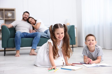 Photo of Kids drawing near their parents on warm floor at home, selective focus. Heating system