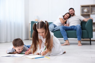 Photo of Kids drawing near their parents on warm floor at home, selective focus. Heating system