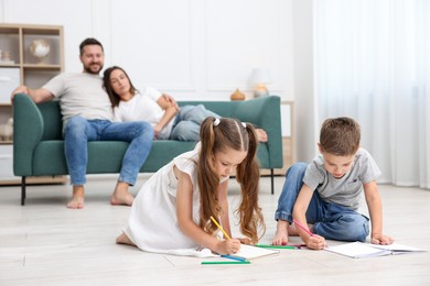 Photo of Kids drawing near their parents on warm floor at home, selective focus. Heating system