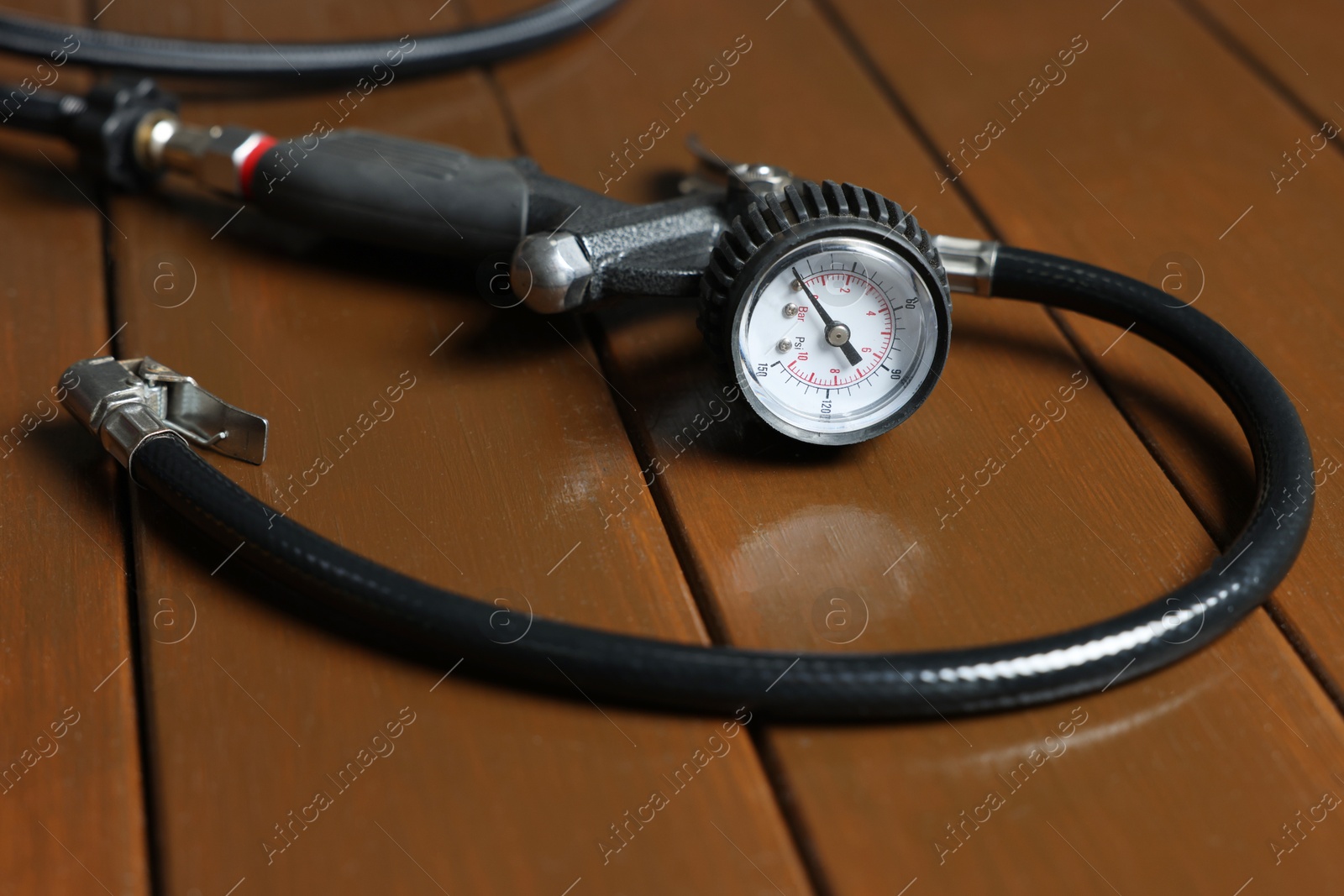 Photo of One tire inflation gun with gauge on wooden background, closeup