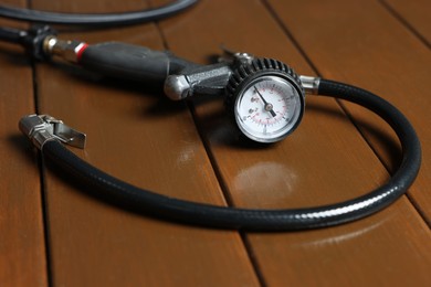 Photo of One tire inflation gun with gauge on wooden background, closeup
