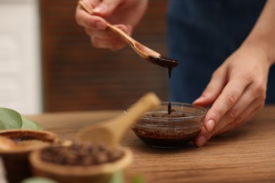 Photo of Woman making natural body scrub at wooden table, closeup