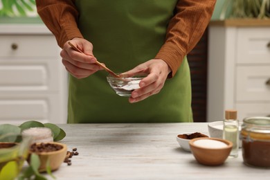 Photo of Making natural scrub. Woman mixing coffee with sugar in bowl at white wooden table, closeup