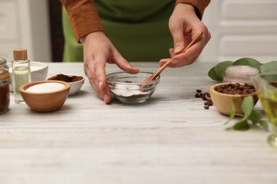 Photo of Making natural scrub. Woman mixing coffee with sugar in bowl at white wooden table, closeup
