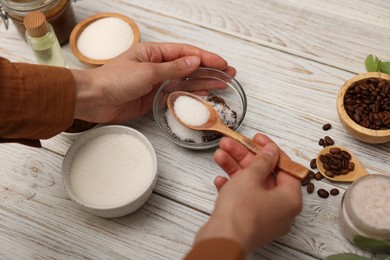 Photo of Making natural scrub. Woman mixing coffee with sugar in bowl at white wooden table, closeup