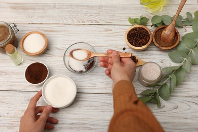 Photo of Making natural scrub. Woman adding sugar into bowl at white wooden table, top view