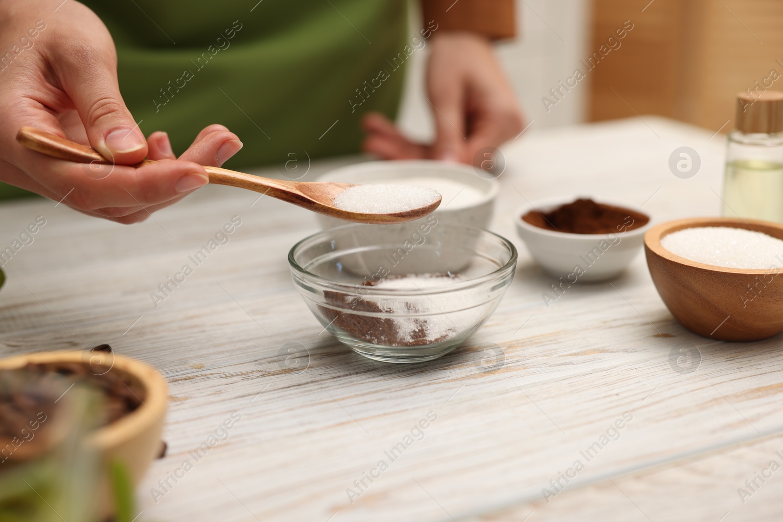 Photo of Making natural scrub. Woman adding sugar into bowl at white wooden table, closeup