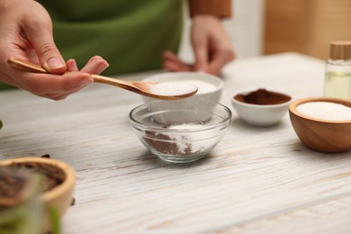 Photo of Making natural scrub. Woman adding sugar into bowl at white wooden table, closeup