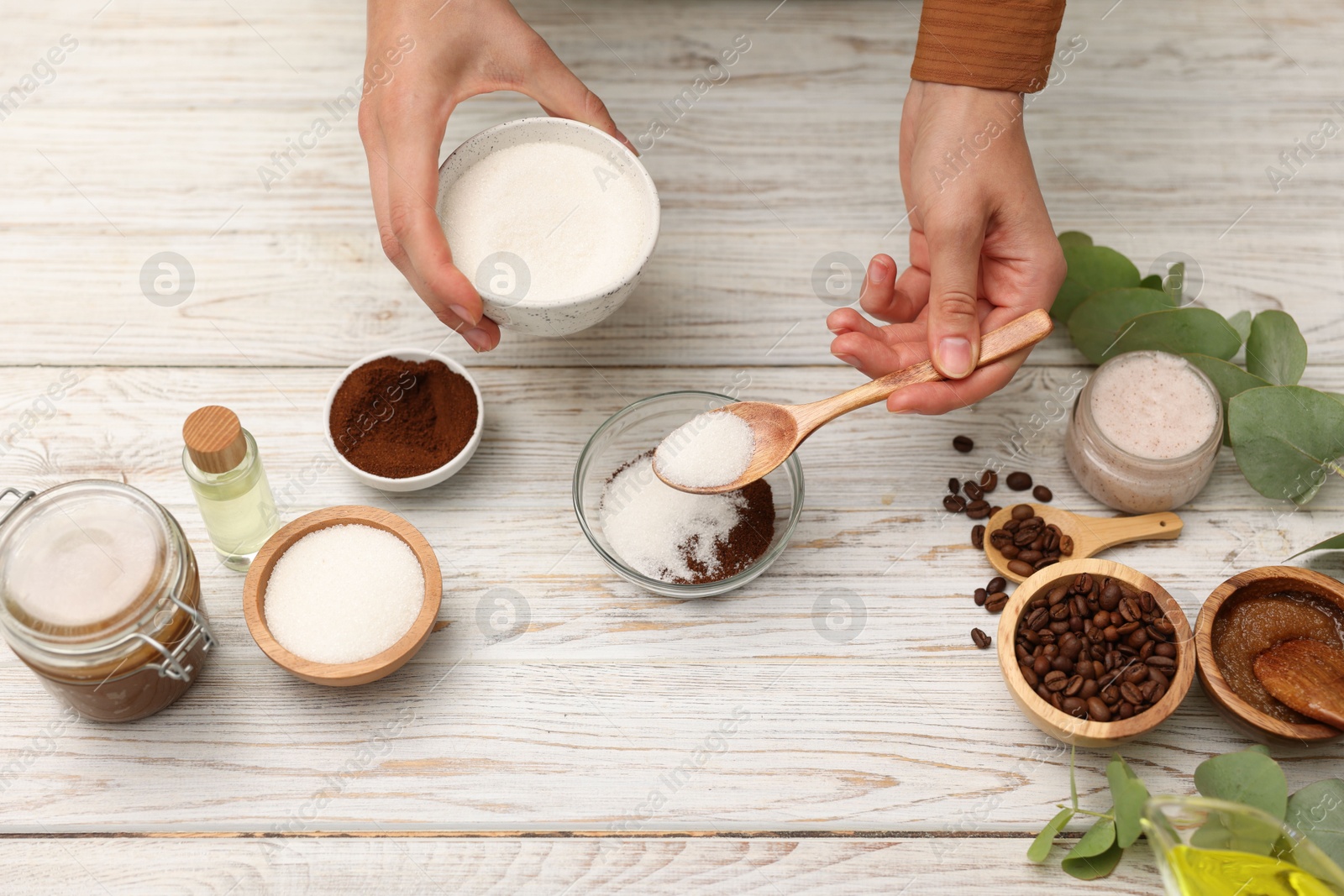 Photo of Making natural scrub. Woman adding sugar into bowl at white wooden table, top view